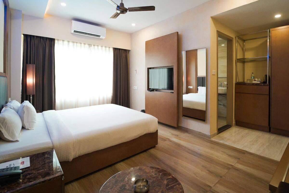 A modern hotel room with a large bed, a TV, a desk, and a bathroom.