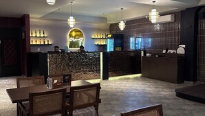 A restaurant with a bar area, wooden tables and chairs, and a projector on the ceiling. - Club Nirvana Boutique Resort Pure-Veg (Sonapur)
