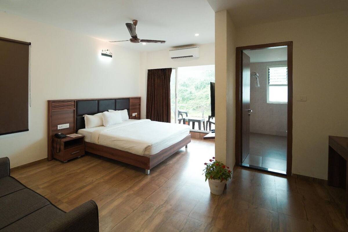 A hotel room with a large bed, a desk, a chair, a ceiling fan, and an air conditioning unit.