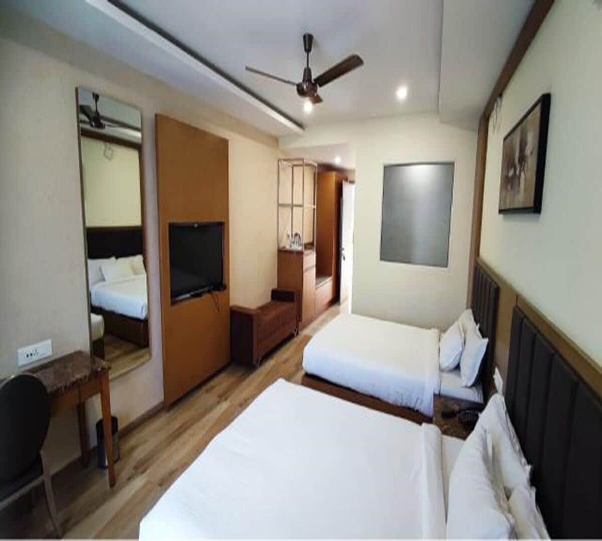 A hotel room with two beds, a TV, a ceiling fan, and a mirror.