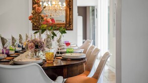 Una mesa de comedor dispuesta con platos, vasos y un jarrón de flores, rodeada de sillas.