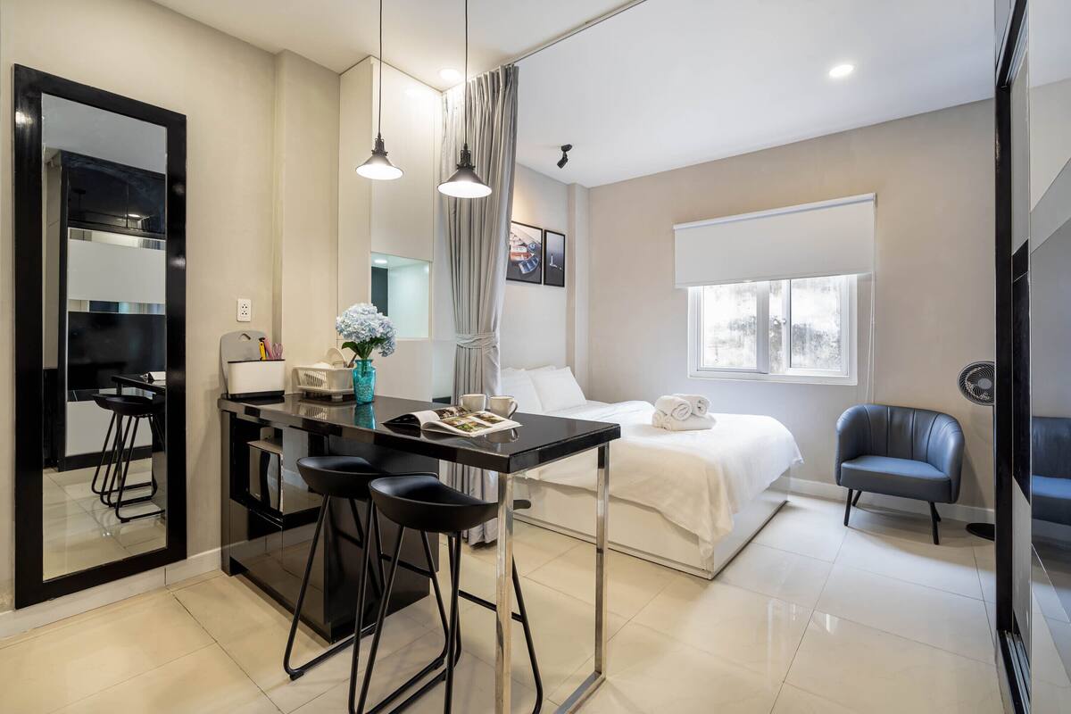 A modern hotel room with a bed, a desk with chairs, a mirror, and a window.