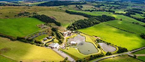 An aerial view of a rural property with a large pond, several buildings, and surrounding green fields.