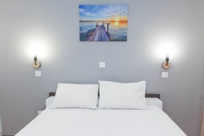 A bedroom with a bed, two bedside tables, and a wall-mounted painting of a sunset over a pier. - Modern Cozy 1 Bd Piraeus Perfection Apt (Piraeus)
