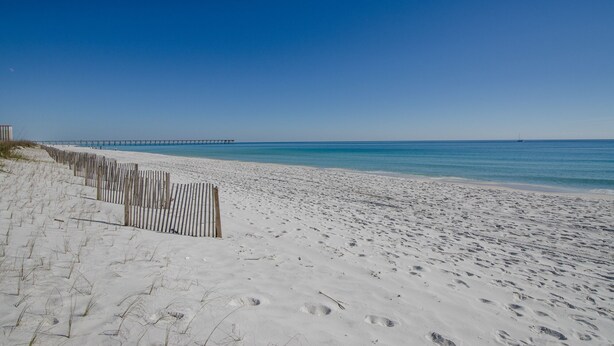 Ein sandiger Strand mit einer Holzzaun und einem Steg im Hintergrund.