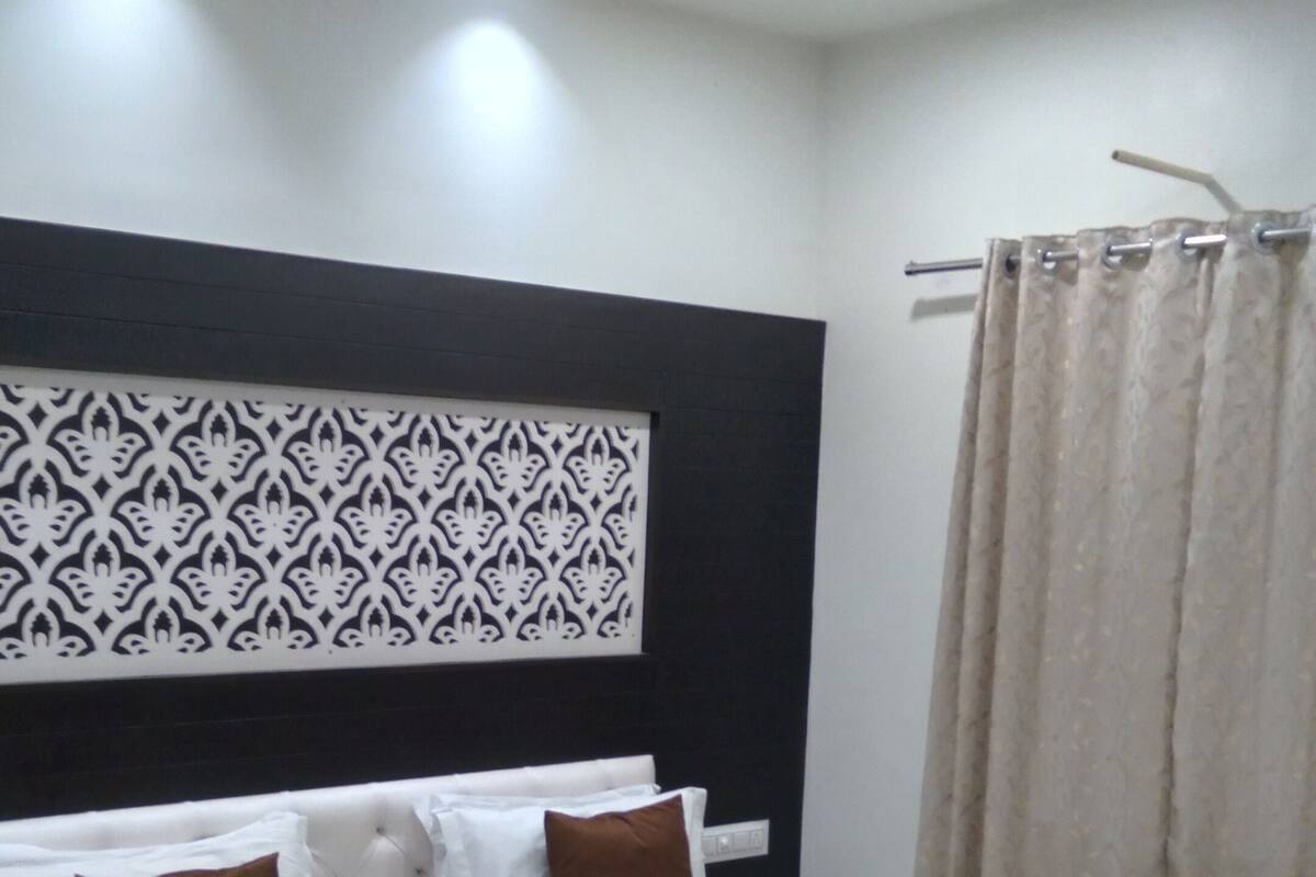 Une chambre à coucher avec un lit, du linge de lit blanc, une tête de lit à motifs, un ventilateur de plafond et un rideau.