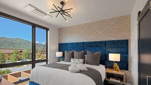 A modern hotel room with a large bed, a view of the outside, and a unique wall design. - Luxury Townhome with Rooftop Spa and Firepit (Steamboat Springs)