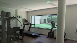 Ein Fitnessstudio mit Cardiogeräten, Gewichten und einem großen Fenster mit Blick auf einen Tennisplatz.
