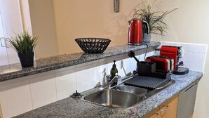 Eine Küche mit Granit-Arbeitsplatten, einer Edelstahl-Spüle, Holzschränken und einem kleinen Topf mit Pflanze.
