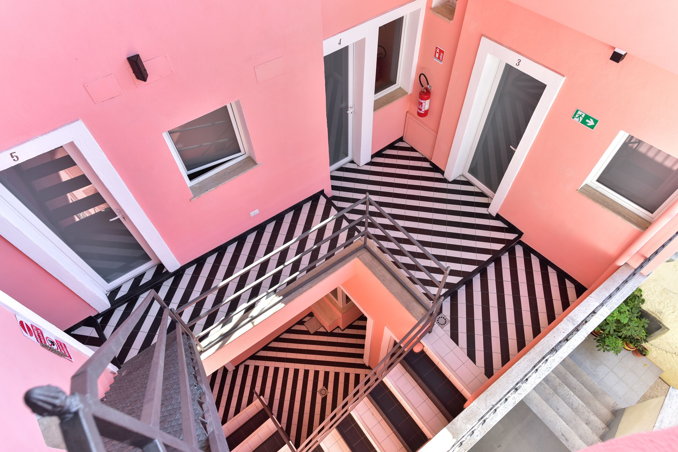 A pink building with a black and white striped floor, multiple doors, and a staircase.