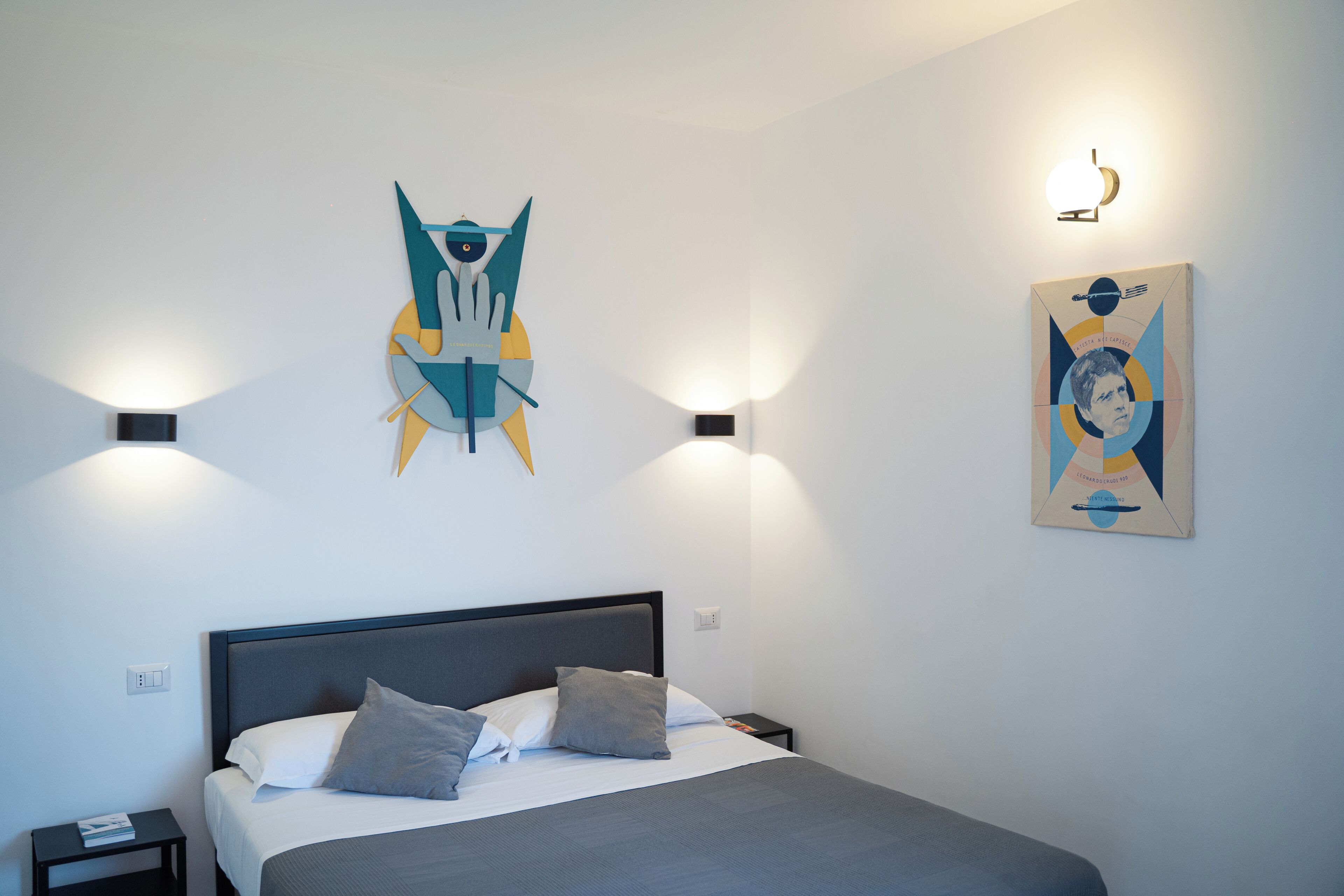 A modern bedroom with a bed, two bedside tables, and abstract wall art.