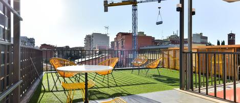 Una terraza en la azotea con sillas amarillas y una mesa, una grúa al fondo y vistas de la ciudad.