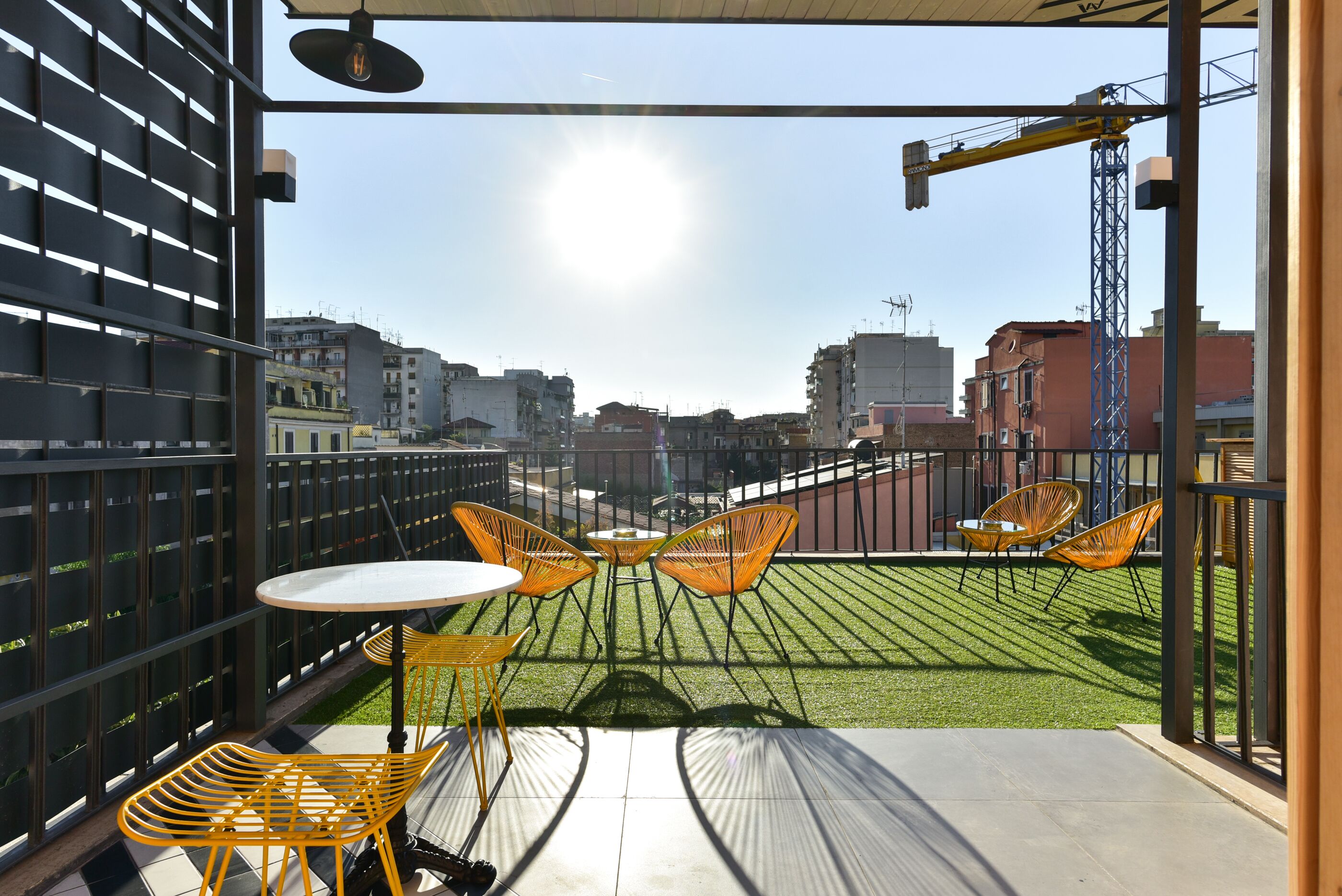 Un balcone con vista sulla città, con un tavolo e sedie, un prato verde e una gru edile sullo sfondo.