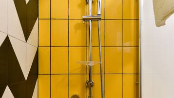 A shower with a chrome hose and a handheld showerhead, set against a yellow tiled wall with a geometric pattern.