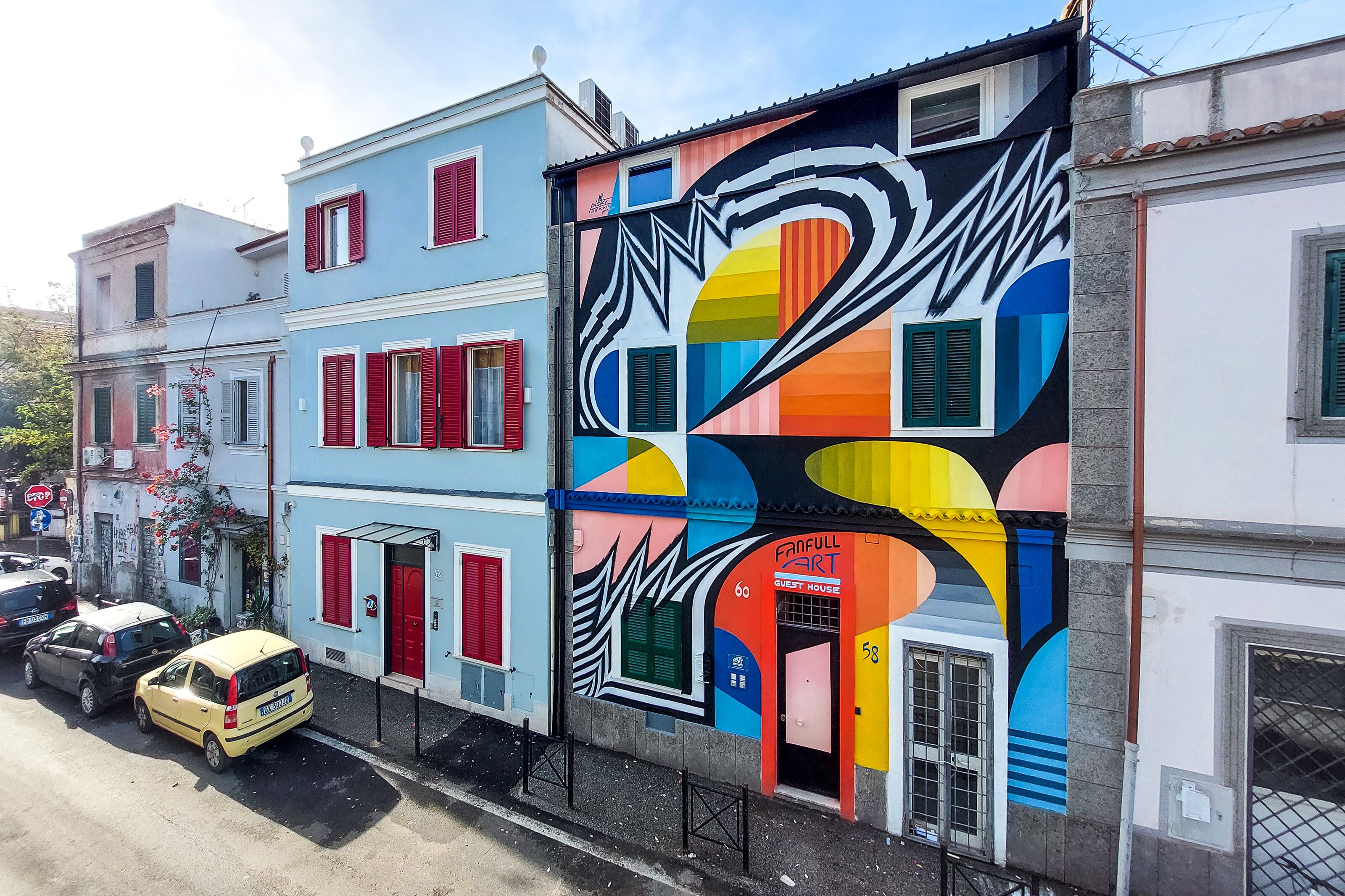 A colorful building with a vibrant mural, a red door, and a sign for Fanfull Art Guest House.
