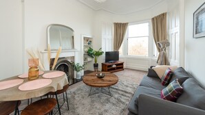 Ein Wohnzimmer mit Kamin, einer Couch, einem Esstisch mit rosa Unterlagen und einem Fernseher.
