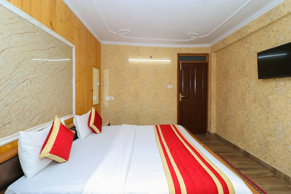 A hotel room with a bed, wooden paneling, a flat-screen TV, and a door.