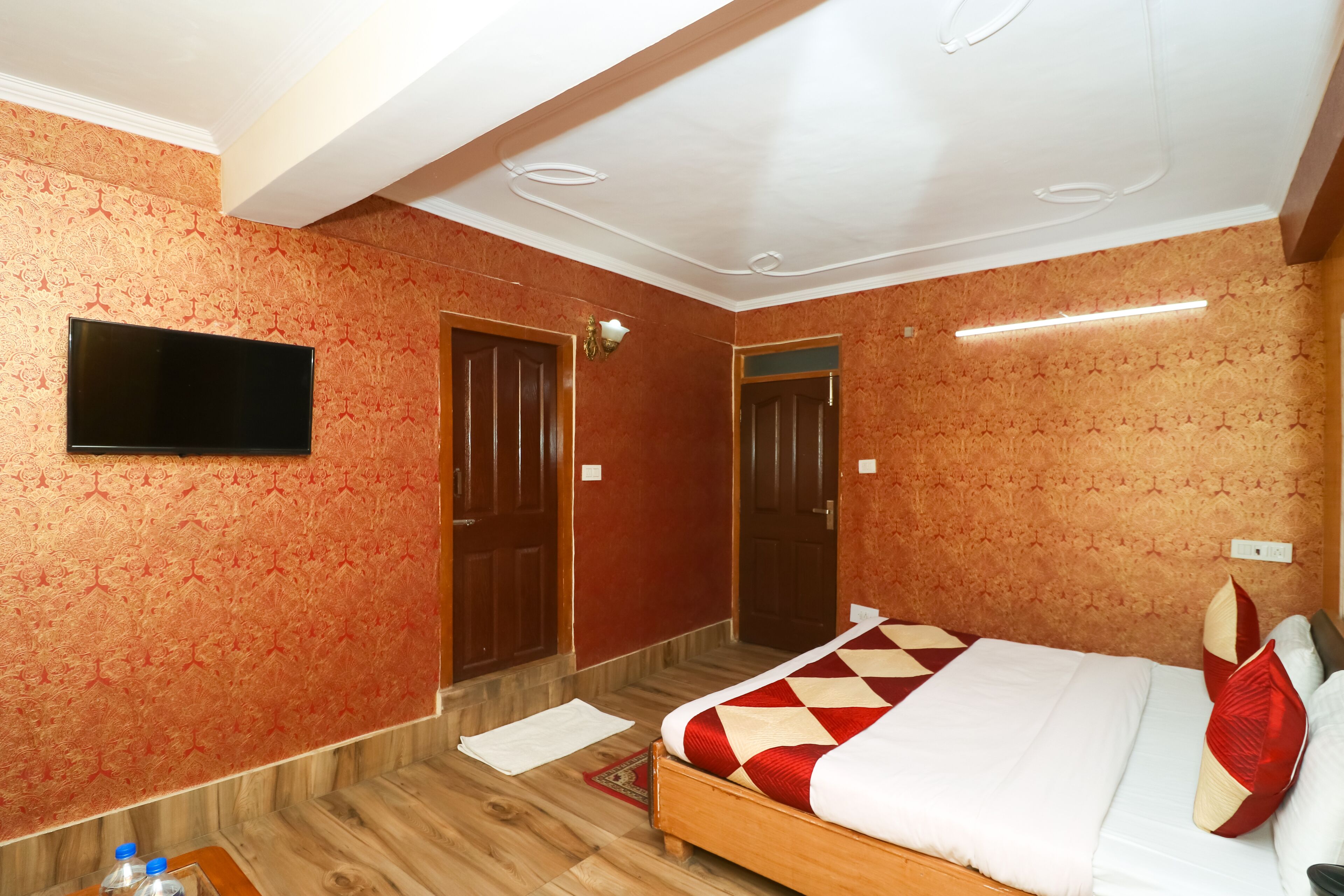 A hotel room with a large bed, a flat-screen TV mounted on the wall, and a wooden floor.
