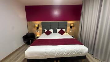 A hotel room with a large bed, two bedside tables with lamps, a chair, and a curtain.