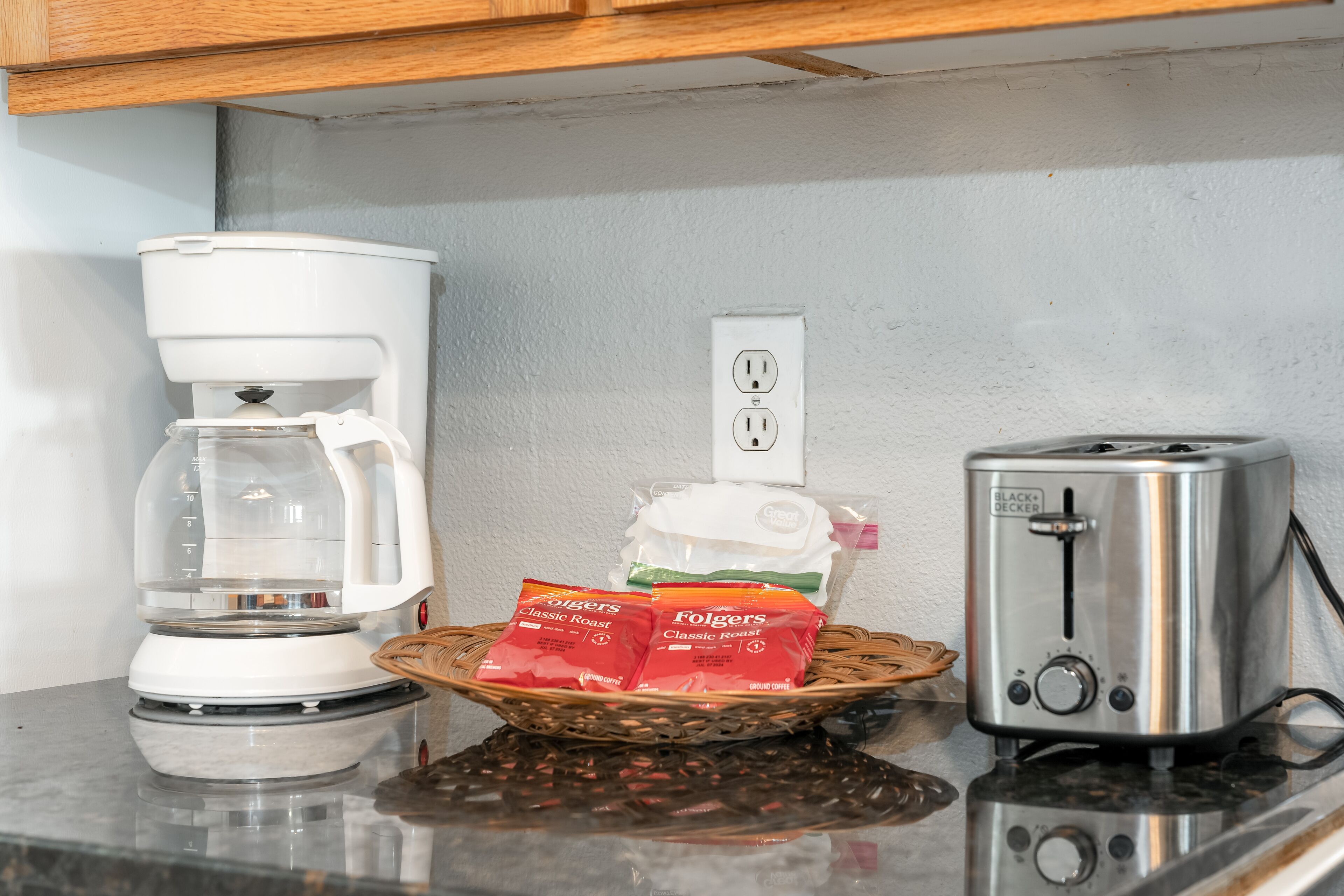 Una encimera de cocina con cafetera, tostadora y una cesta con sobres de café Folgers.
