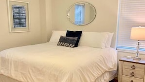 Un dormitorio con una cama grande, un ventilador de techo, una mesita de noche con lámpara y una ventana con persianas.