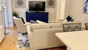 Una sala de estar con un sofá color beige, una mesa de centro y un televisor de pantalla plana sobre un mueble azul.
