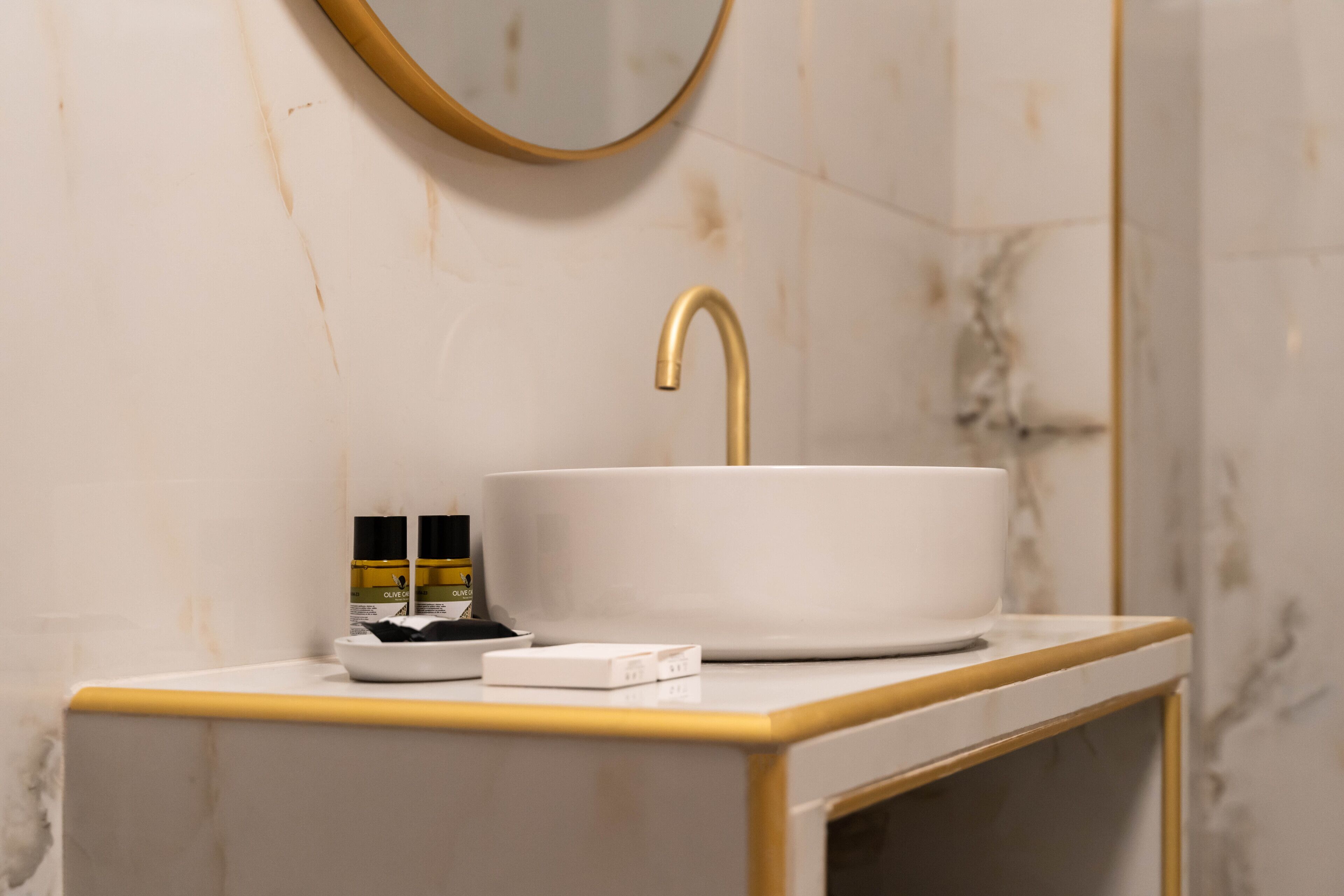 Ein Badezimmer mit einem weißen Marmorbecken, einem goldenen Wasserhahn und einem Spiegel.