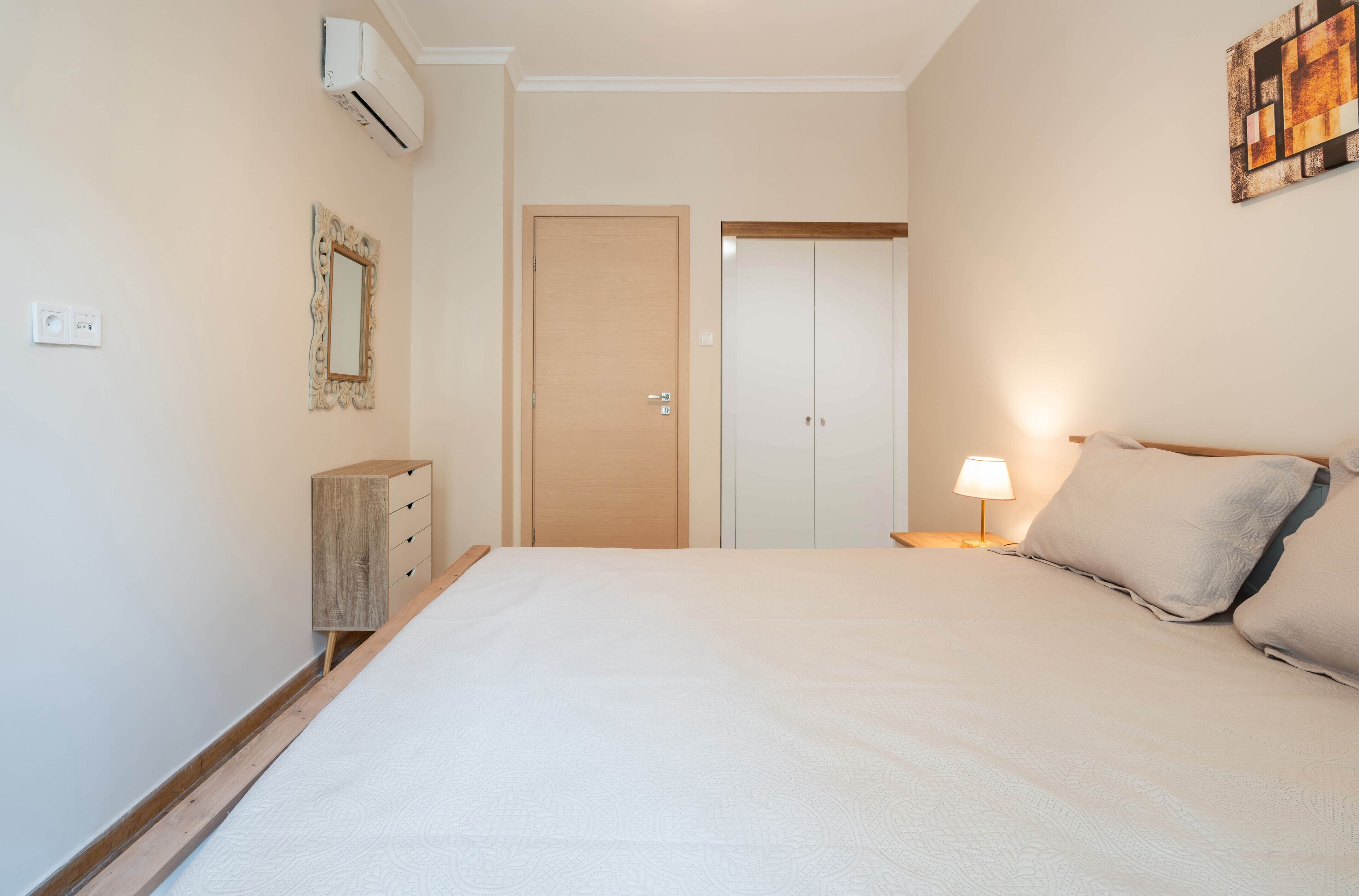 A bedroom with a bed, bedside lamp, wardrobe, and an air conditioning unit.