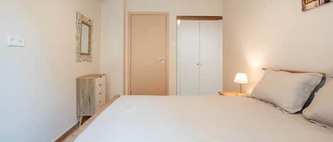 A bedroom with a bed, bedside lamp, wardrobe, and an air conditioning unit.