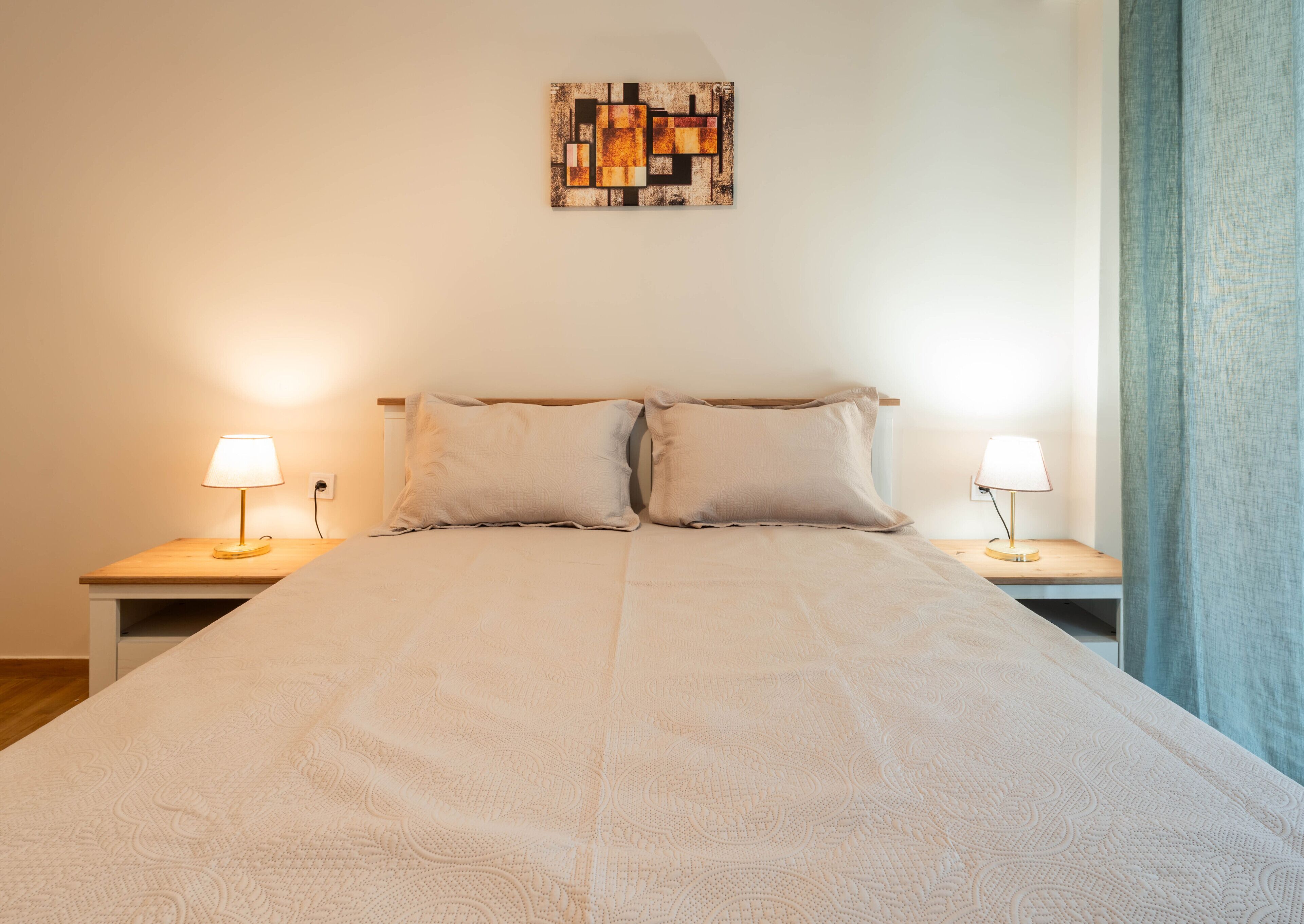 A neatly made bed with a patterned bedspread, two pillows, and bedside lamps on wooden nightstands.