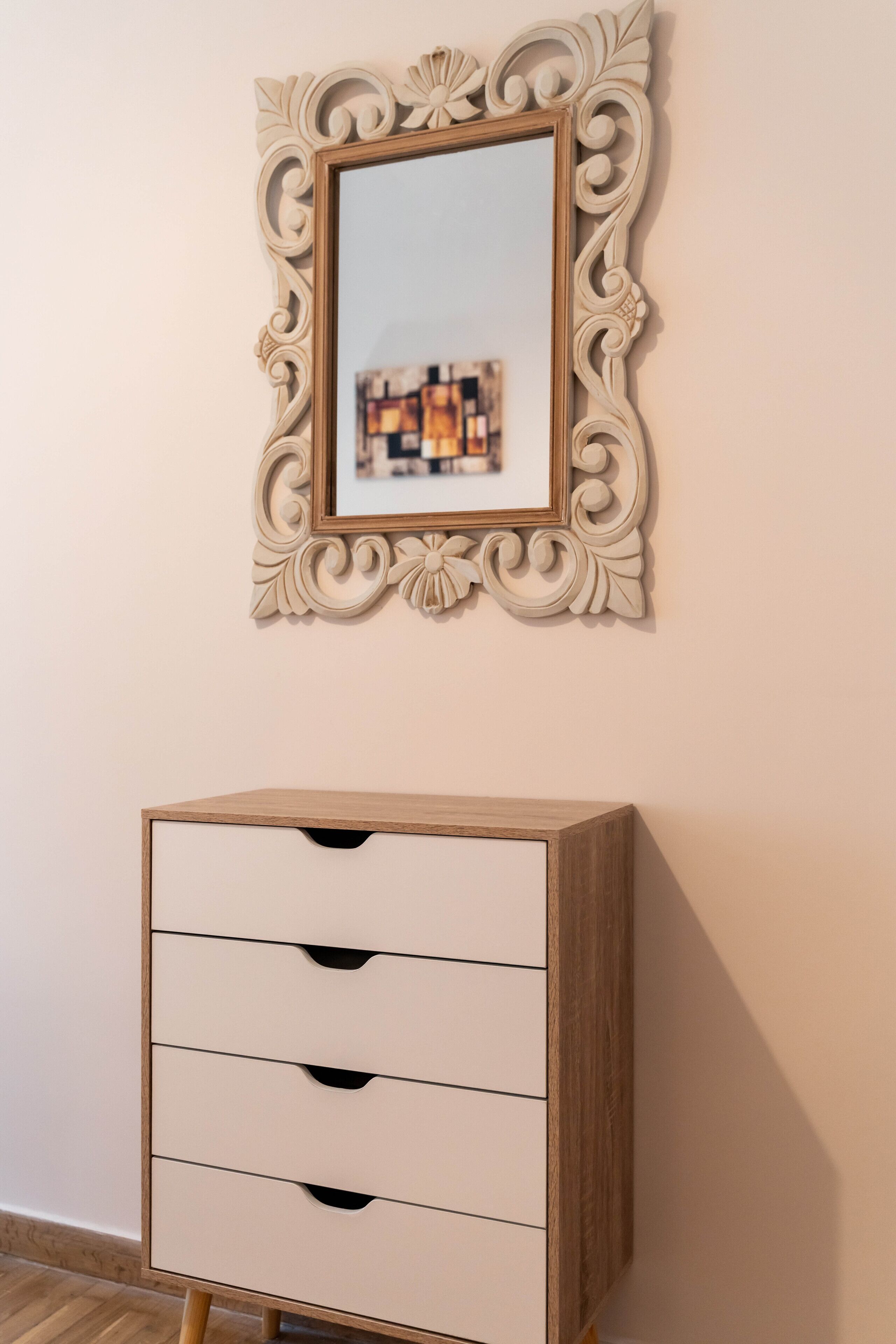 A wooden dresser with four drawers and a mirror with an ornate frame.