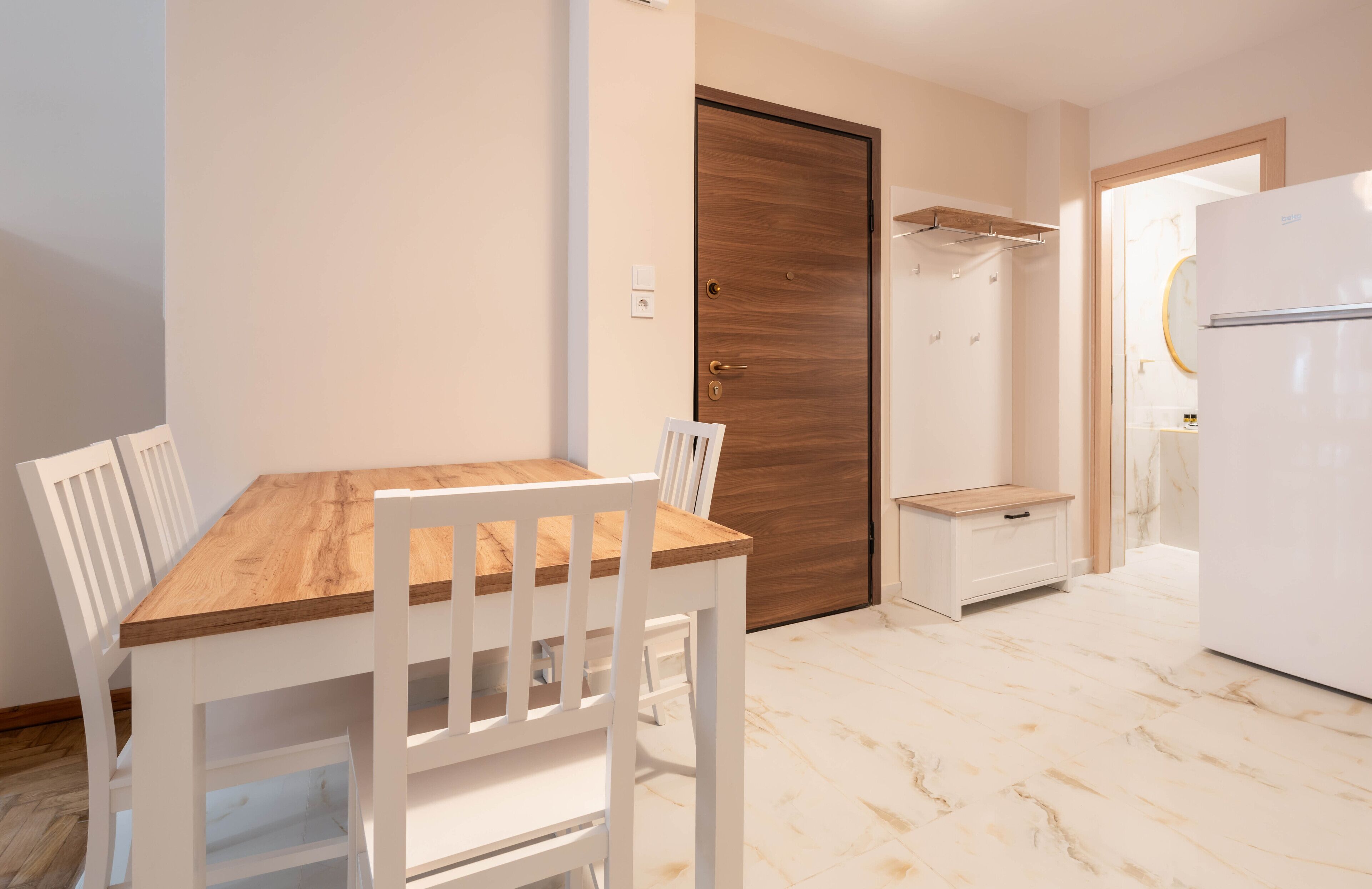 A kitchen with a wooden table and white chairs, a white refrigerator, and a wooden door.