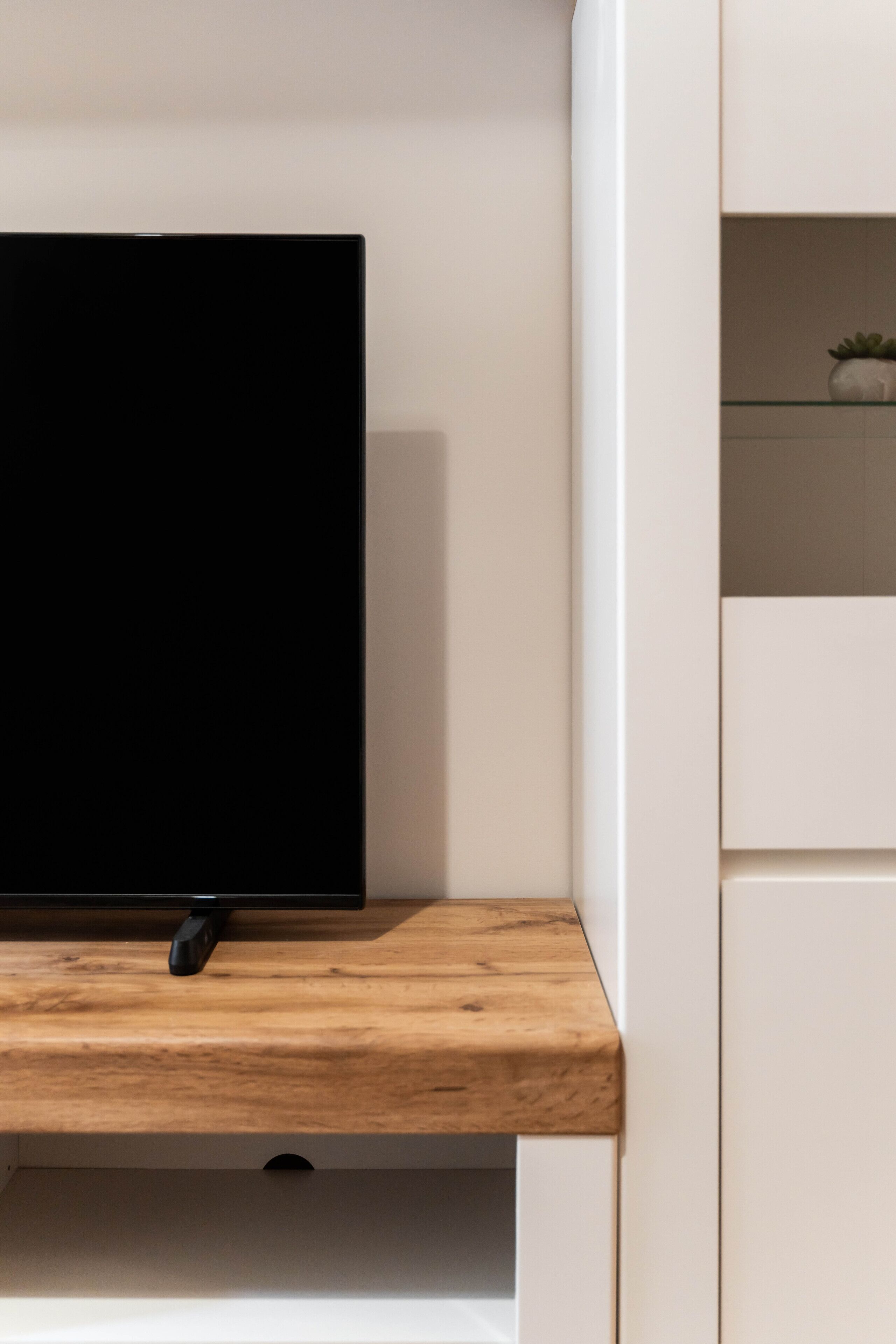 Ein modernes Zimmer mit einem an einer Holzhilfe befestigten Flachbildfernseher, einer weißen Wand und einem kleinen Topfpflanzen auf einem Regal.