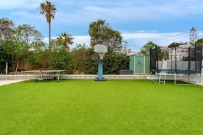 Un patio trasero con canasta de baloncesto, un trampolín y una mesa de tenis de mesa.