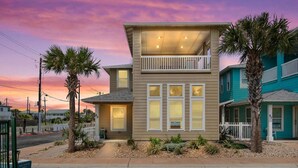 A two-story house with a balcony, surrounded by palm trees and a sunset sky. - "Escape to Palm SunDaze, where the soothing ocean breeze melts your cares away, embracing you in the tranquility of coastal living. (Port Aransas)