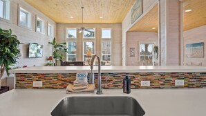 A modern kitchen with a central island, a built-in bookshelf, and a large window. - "Escape to Palm SunDaze, where the soothing ocean breeze melts your cares away, embracing you in the tranquility of coastal living. (Port Aransas)