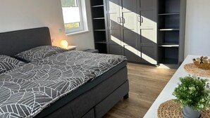A bedroom with a bed, a bedside table with a lamp, a wardrobe, and a small table with a plant. - Exklusive Ferienwohnung bei Berlin, bis 5 Gäste, Große Terrasse, Garten (Bestensee)