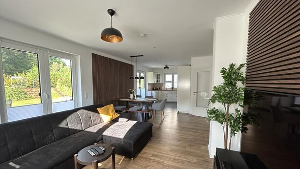 A modern living room with a dark sofa, a small round table, and a large window. - Exklusive Ferienwohnung bei Berlin, bis 5 Gäste, Große Terrasse, Garten (Bestensee)