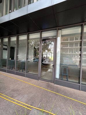 A modern building with large glass windows and a door, reflecting a car and trees. - One Bedroom Studio Apartment at The Lennox Airport Residential Accra (Accra)