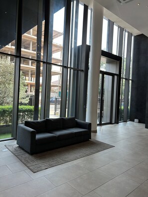 A modern interior with a sofa, large windows, and a view of the outside. - One Bedroom Studio Apartment at The Lennox Airport Residential Accra (Accra)