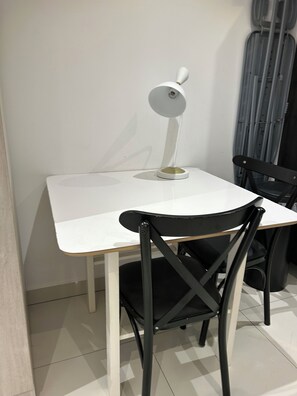 A white table with a modern lamp, two black chairs, and a grey curtain in the background. - One Bedroom Studio Apartment at The Lennox Airport Residential Accra (Accra)