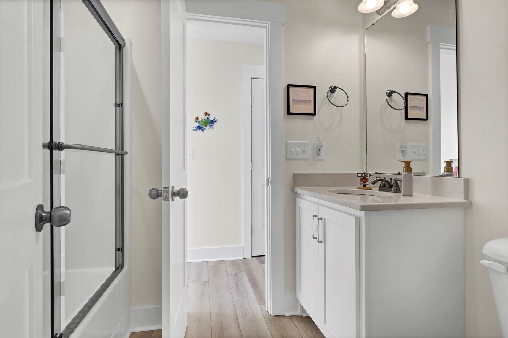 A bathroom with a white sink, a mirror, and a toilet. There is a door leading to another room.