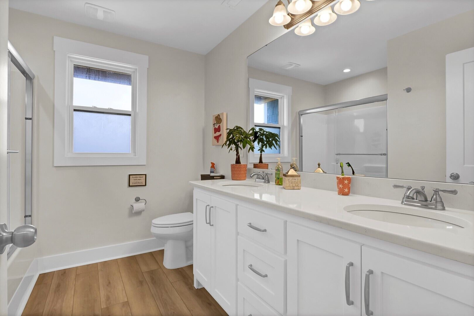 A modern bathroom with white cabinetry, a large mirror, and a window.