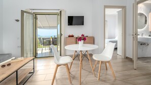 Una sala de estar moderna con una mesa redonda, sillas blancas, un televisor de pantalla plana y un ventanal que da a un balcón.