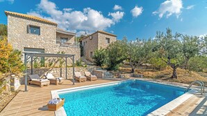 Una villa de piedra con piscina, sillones de exterior y una pérgola.