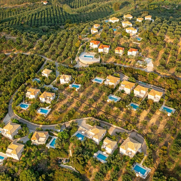 An aerial view of a residential area with houses, swimming pools, and a hilly landscape.