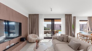 Un salon moderne doté d’un grand téléviseur à écran plat, d’un canapé confortable, d’une table basse blanche et d’un coin repas avec une table et des chaises.