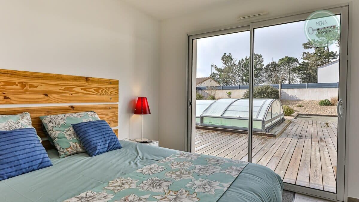 A bedroom with a wooden headboard, a bed with floral bedding, a red lamp, and a sliding glass door leading to a wooden deck.