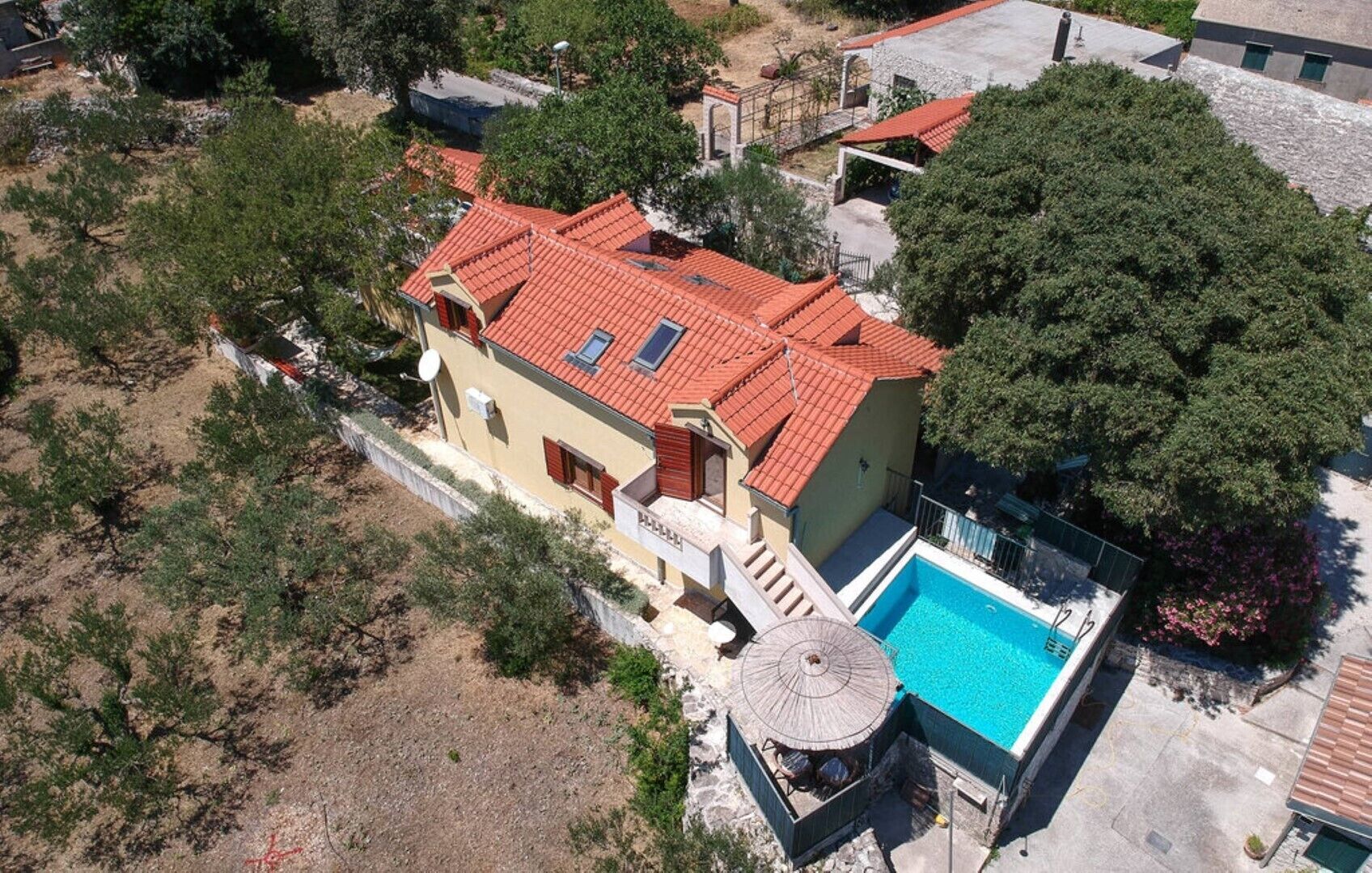 A two-story house with a red-tiled roof, a swimming pool, and a small garden area.