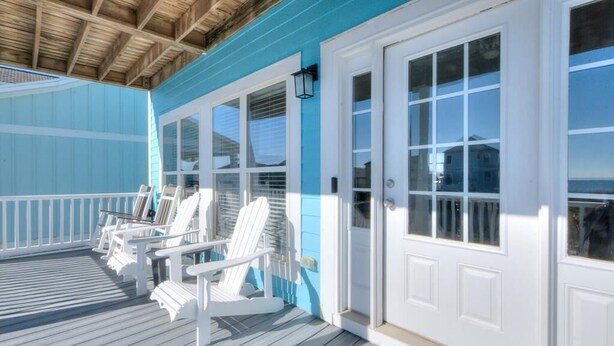 En overdækket veranda med hvide Adirondack-stole, en blå facade og en hvid dør med et vindue.